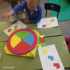 two children are sitting at a table with paper cutouts and colored shapes on them