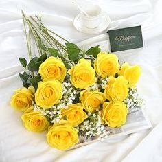 a bouquet of yellow roses and baby's breath next to a card on a bed