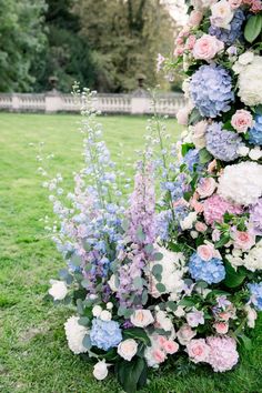 an arrangement of flowers on the grass in front of a white picket fence with blue and pink blooms