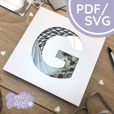 the letter g is cut out from paper and surrounded by crafting supplies on a table