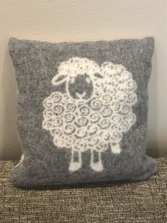 a gray and white sheep pillow sitting on top of a couch next to a wall