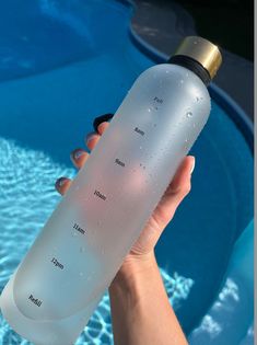 a hand holding a water bottle in front of a swimming pool