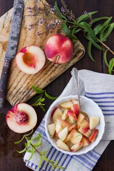 a bowl filled with sliced peaches on top of a wooden cutting board next to a knife