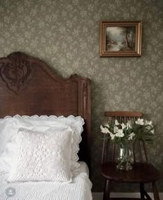 a bed with white sheets and pillows next to a small table with flowers in it