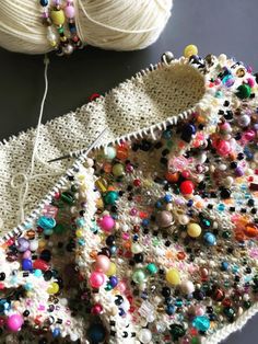 two balls of yarn are next to a crocheted sweater with beads on it