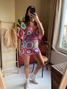 a woman taking a selfie while wearing a colorful crochet dress and white tennis shoes