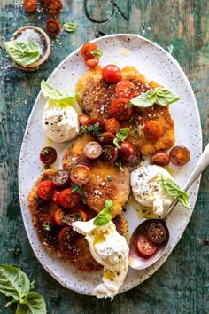 a white plate topped with meat covered in tomatoes and mozzarella next to a fork