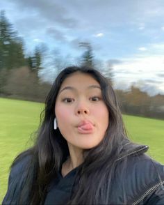 a woman making a funny face while standing in front of a green field with trees