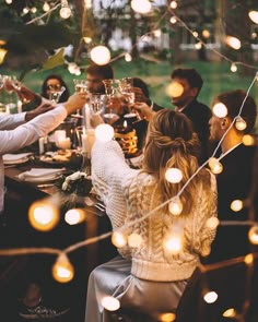 a group of people sitting around a dinner table with lights strung from the ceiling above them