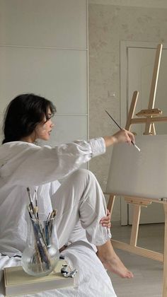 a woman sitting in front of an easel painting