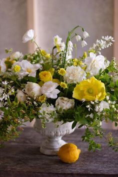 a vase filled with white and yellow flowers on top of a wooden table next to a lemon