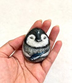 a hand holding a small painted rock with a bird on it's face in front of a white background