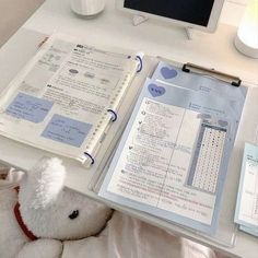 a teddy bear is sitting next to an open book on a desk with other items