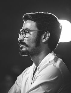 a black and white photo of a man with glasses looking off to the side in front of a light