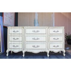 an antique dresser with white paint and gold trimmings on the drawers is displayed in front of a painting