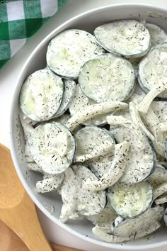 a bowl filled with sliced up eggplant next to a wooden spoon and green checkered napkin