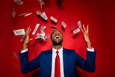 a man in a suit and red tie is surrounded by money falling from his hands