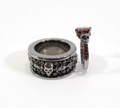 two wedding rings with black and red stones on them, one is in the shape of a skull