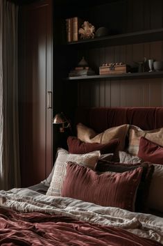 a bed with red sheets and pillows in a room next to a book shelf filled with books