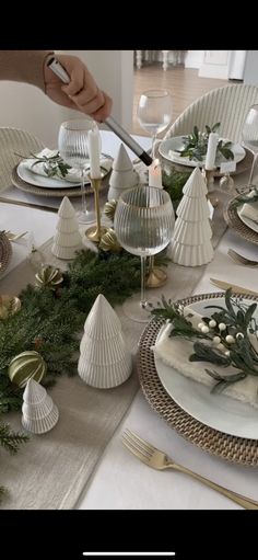 the table is set for christmas dinner with white plates and silverware, greenery and candlesticks