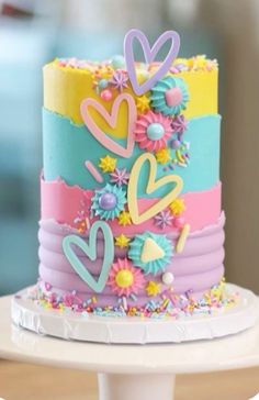 a multicolored cake with flowers and hearts on top is sitting on a table