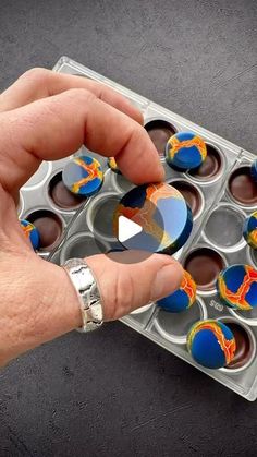 a person holding an open muffin tin filled with blue and orange cupcakes