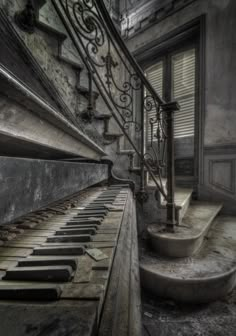 an old piano sitting in the middle of a room next to a stair case and window