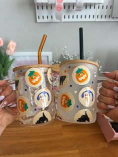 two people holding up coffee cups with pumpkins and cats on them, sitting at a table