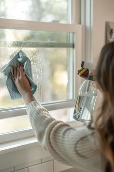 a woman is cleaning the window with a rag and spray bottle in her left hand