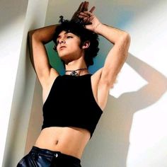 a woman in black top and leather shorts posing for the camera with her hands behind her head