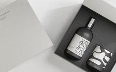 a bottle of wine in a black box next to a white paper package with an abstract design on it