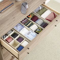 an open drawer with ties and other items in it on a wooden table next to a bed