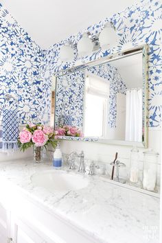 a blue and white bathroom with flowers on the counter top, large mirror over the sink