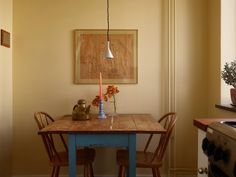 a kitchen table with two chairs and a painting on the wall above it, in front of a stove