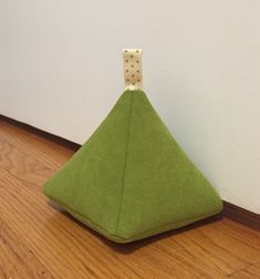 a green triangle shaped object sitting on top of a hard wood floor next to a white wall