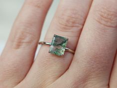 a woman's hand with a ring that has an emerald colored stone in it