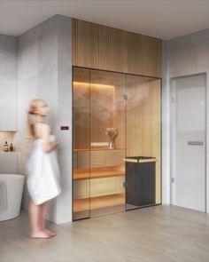 a woman in a white bathrobe walking into a bathroom with a large glass door