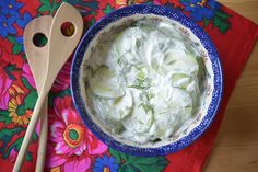 a blue bowl filled with cucumber and sour cream next to a wooden spoon