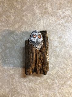 an owl brooch sitting on top of a piece of drift wood with eyes wide open