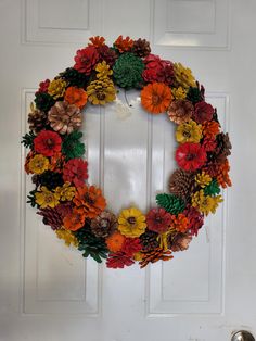 a wreath made out of pine cones and flowers on the front door with a bell