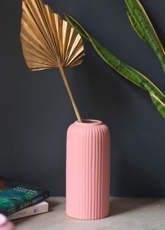 a pink vase sitting next to a green plant