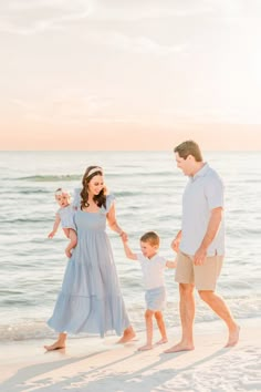 a family walking on the beach at sunset with their toddler holding his mom's hand