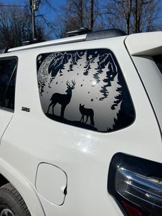 a white car with a deer decal on it's windshield and trees in the background