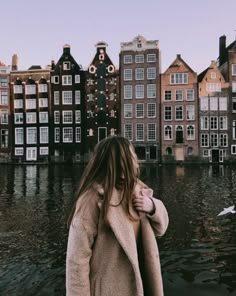 a woman standing on the edge of a body of water with buildings in the background