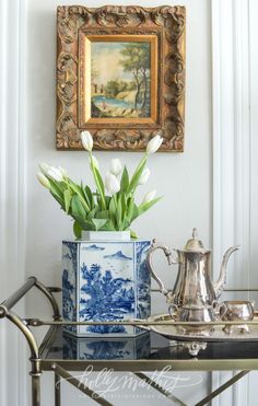 tulips in a blue and white vase on a glass table next to a painting