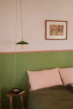 a bed with green and pink sheets in a bedroom next to a painting on the wall