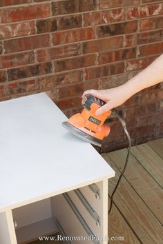 a person using a sander on a white table with brick wall in the background