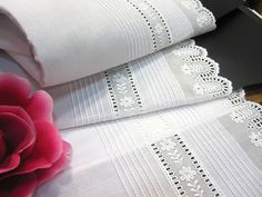 two white bedspreads and a pink flower on top of each other with lace trim