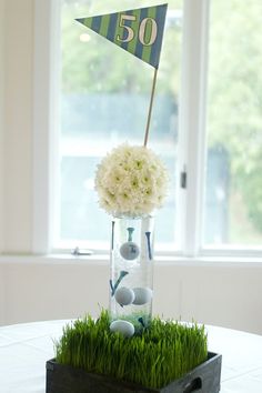 a vase filled with flowers and golf balls sitting on top of a wooden table next to a window