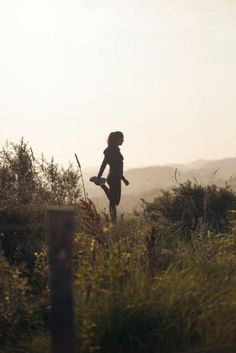 a woman is running through the grass with her back to the camera and she has one leg in the air